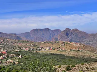 Bergdörfer in einer hügeligen Landschaft vor den hohen Bergen des Antiatlas unter blauem Himmel