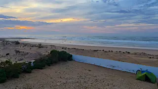 Strandabschnitt mit einem niedrigen weißen Wall und einem Zelt auf dem Campingplatz bei bewölktem Himmel und ruhiger See