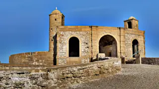 Steinerne Wehranlage mit zwei runden Türmen und großen Rundbogenfenstern vor blauem Himmel in Essaouira