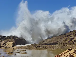 Brandung schlägt gegen felsige Küste bei Imsouane unter blauem Himmel