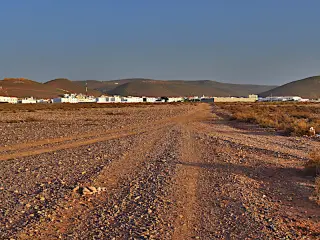 Schotterpiste führt durch karge Landschaft zum Ort Mirleft vor niedrigen Hügeln