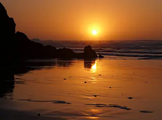 Sonnenuntergang über einem Strand bei Mirleft mit Felsen und spiegelnder Wasseroberfläche