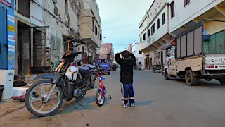 Junge steht auf einer Straße im Stadtbezirk Trabsini vor einem Motorrad und einem kleinen Fahrrad mit den Händen am Kopf