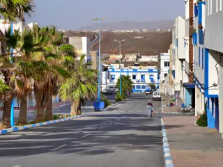 Straße in Sidi Ifni mit Palmen am linken Rand, mehrstöckigen Gebäuden rechts und einem blauen Hotelgebäude im Hintergrund