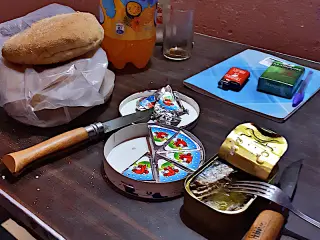 Käseportionen in runder Verpackung, geöffnete Sardinenbüchse mit Gabel,  2Messer , Brötchen in Tüte, Getränkeflasche auf Tisch