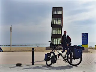 Die Skulptur L’estel ferit mit vier versetzt übereinander gestapelten, schmalen Kuben am Strand von Barcelona, davor ein Fahrrad mit Packtaschen