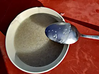 Schale mit Grießsuppe und Löffel auf rotem Untergrund