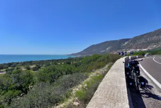 Ein Fahrrad steht auf einer Küstenstraße nach Agadir mit Blick auf das Meer und die grünen Hügel im Hintergrund