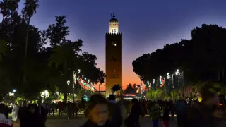 Die Koutoubia-Moschee in Marrakesch bei Dämmerung mit beleuchteten Straßenlaternen und Menschen auf dem Platz davor