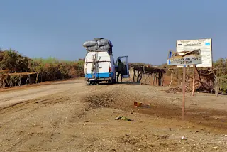 Unbefestigte Straße an der Grenze zu Senegal mit einem Lastwagen, einem Mann neben dem Fahrzeug und Schildern am Straßenrand