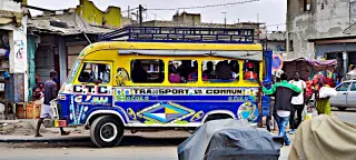 Bunter Minibus steht in einer belebten Straße von Dakar, umgeben von mehreren Personen und Gebäuden im Hintergrund