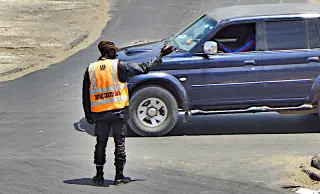 Polizist mit orangefarbener Warnweste steht auf einer Straße und regelt den Verkehr vor einem blauen Geländewagen in Dakar