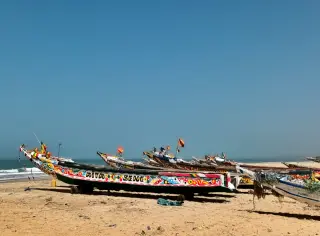 Mehrere bunt bemalte, traditionelle senegalesische Fischerboote liegen auf einem Sandstrand unter klarem Himmel