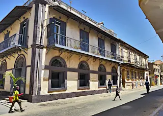 Straße in St. Louis mit einem Gebäude im Kolonialstil, mit Balkone und mehrere Fenster, auf der Straße gehen mehrere Personen