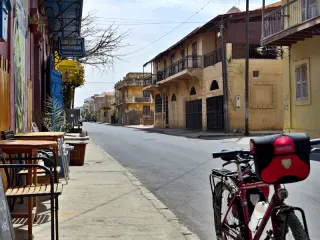 Leere Straße in St. Louis im Senegal mit Fahrrad und Café-Tischen auf dem Bürgersteig neben bunten Häusern